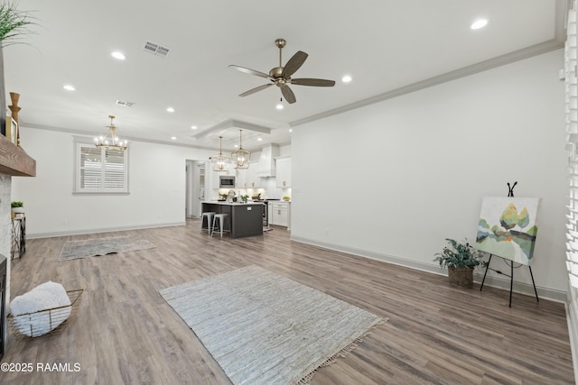 living room featuring ceiling fan with notable chandelier, wood-type flooring, and crown molding