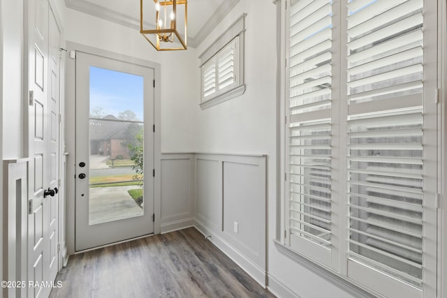 doorway to outside with dark wood-type flooring, crown molding, and an inviting chandelier