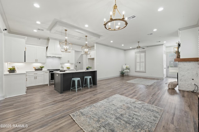 kitchen featuring premium range hood, ceiling fan, decorative light fixtures, a center island with sink, and white cabinets