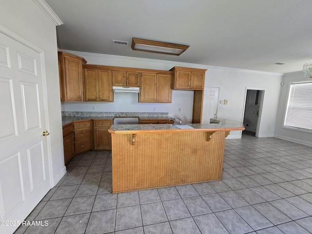 kitchen with sink, a breakfast bar, light tile patterned floors, a center island with sink, and ornamental molding