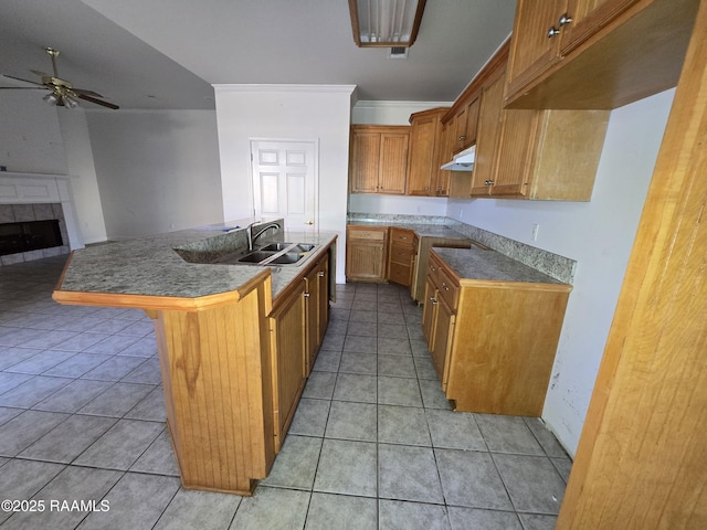 kitchen with a tile fireplace, ceiling fan, sink, a kitchen breakfast bar, and a center island with sink