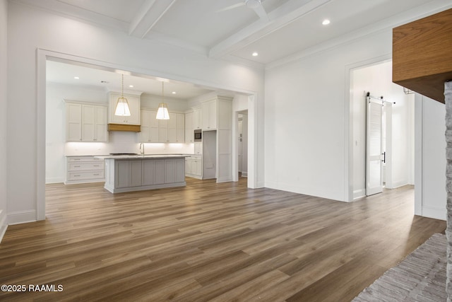 kitchen featuring white cabinets, a barn door, an island with sink, decorative light fixtures, and beam ceiling