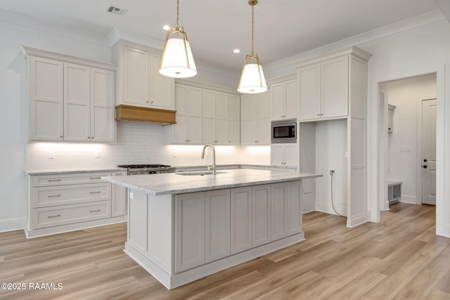 kitchen with sink, decorative light fixtures, a center island with sink, light hardwood / wood-style floors, and stainless steel microwave