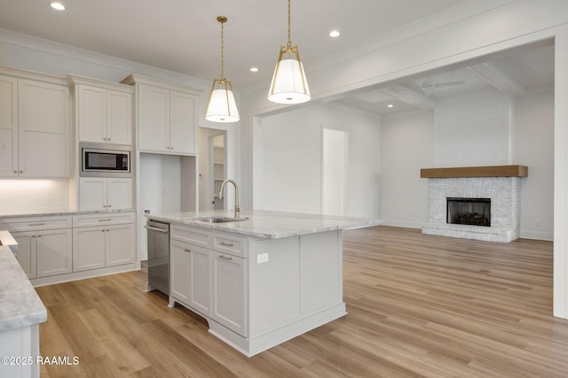 kitchen featuring light stone countertops, sink, decorative light fixtures, a fireplace, and an island with sink