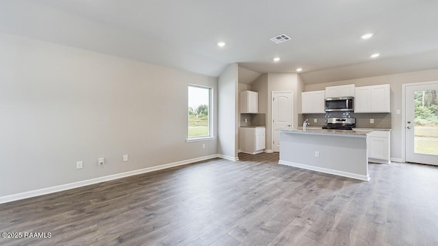 kitchen with lofted ceiling, a center island with sink, light stone counters, white cabinetry, and stainless steel appliances