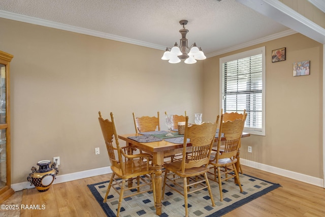 dining space with light hardwood / wood-style floors, ornamental molding, a textured ceiling, and an inviting chandelier