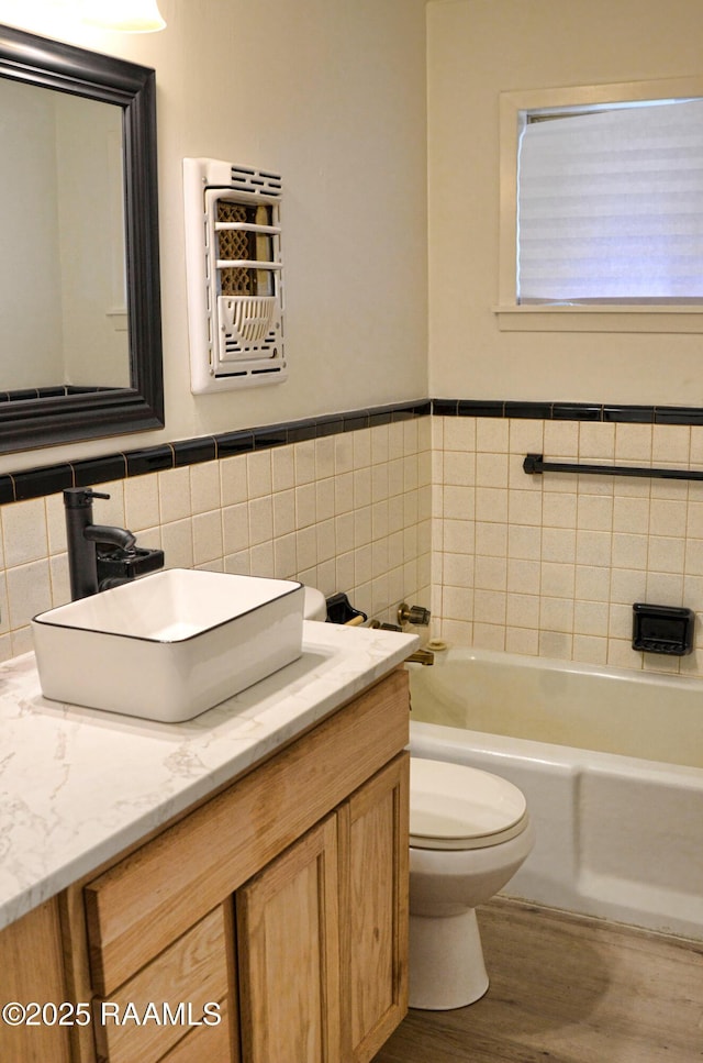 bathroom with toilet, tile walls, vanity, a tub, and hardwood / wood-style flooring