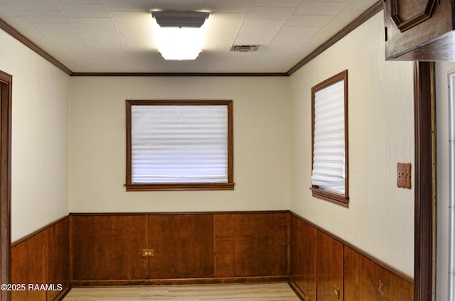 empty room with wooden walls, ornamental molding, and light wood-type flooring