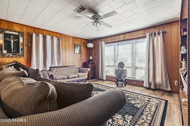 living room with ceiling fan, wood walls, and light wood-type flooring