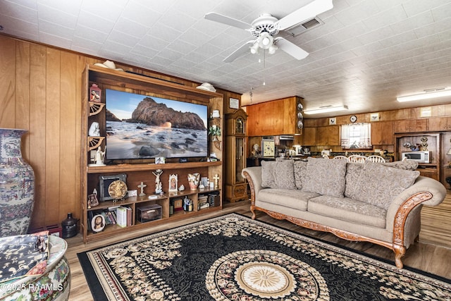 living room with ceiling fan, light hardwood / wood-style floors, and wooden walls