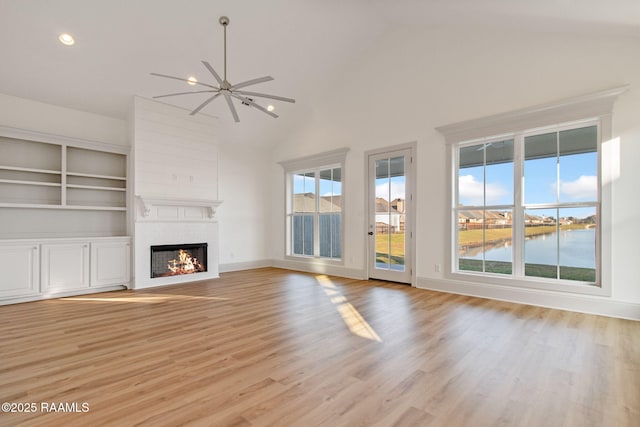 unfurnished living room with built in shelves, ceiling fan, light hardwood / wood-style flooring, vaulted ceiling, and a water view