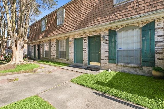 exterior space with mansard roof, a shingled roof, and brick siding