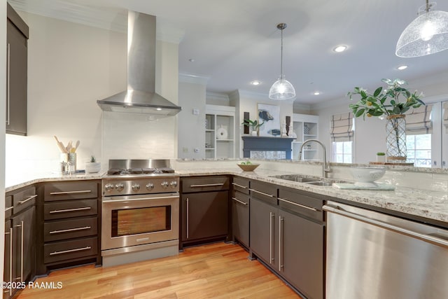 kitchen featuring hanging light fixtures, sink, wall chimney exhaust hood, light stone countertops, and appliances with stainless steel finishes