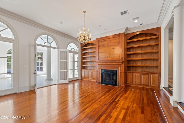 unfurnished living room featuring an inviting chandelier, wood-type flooring, ornamental molding, and ornate columns