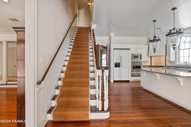 staircase featuring an inviting chandelier, hardwood / wood-style floors, crown molding, and decorative columns