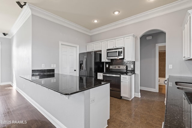 kitchen with kitchen peninsula, appliances with stainless steel finishes, dark stone counters, dark tile patterned floors, and white cabinetry