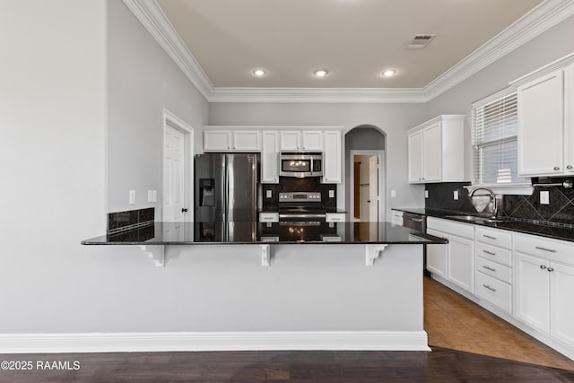 kitchen with appliances with stainless steel finishes, a kitchen breakfast bar, sink, dark stone countertops, and white cabinets