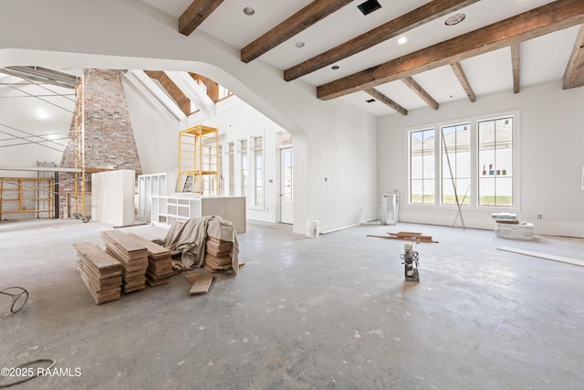 unfurnished living room featuring beam ceiling, concrete floors, and a towering ceiling