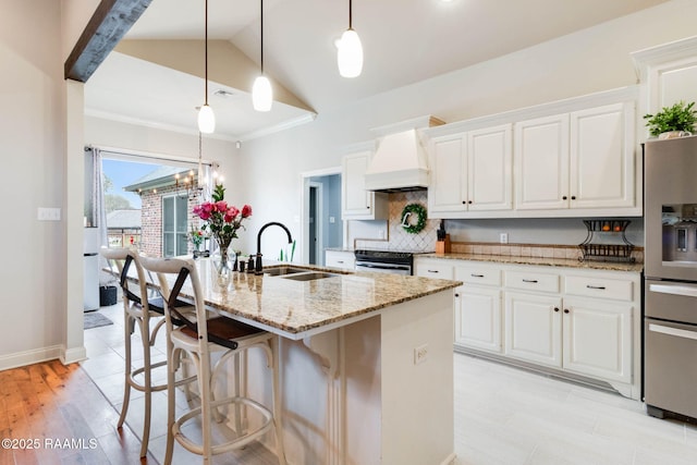 kitchen with light stone countertops, an island with sink, decorative light fixtures, white cabinets, and custom range hood