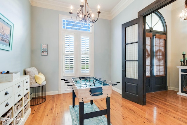 rec room featuring crown molding, light hardwood / wood-style flooring, a chandelier, and french doors