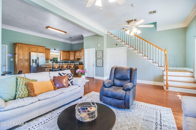 living room with ceiling fan, light hardwood / wood-style flooring, a textured ceiling, and ornamental molding