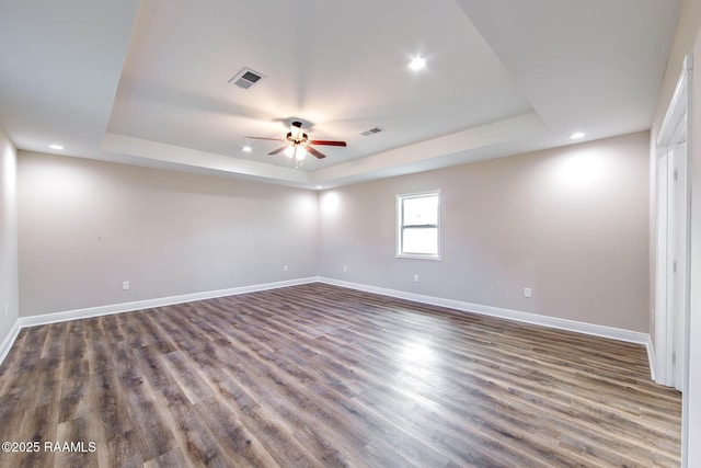 unfurnished room with a tray ceiling, ceiling fan, and dark wood-type flooring