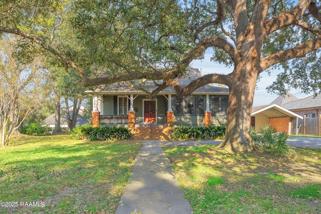 view of property hidden behind natural elements featuring a carport, a porch, and a front yard