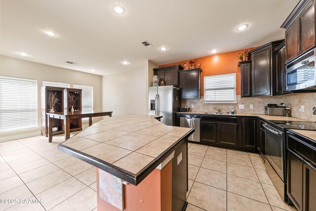 kitchen featuring light tile patterned flooring, stainless steel appliances, a center island, and tasteful backsplash