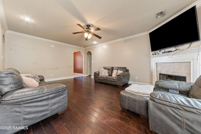 living room with a tiled fireplace, ornamental molding, ceiling fan, and dark hardwood / wood-style flooring