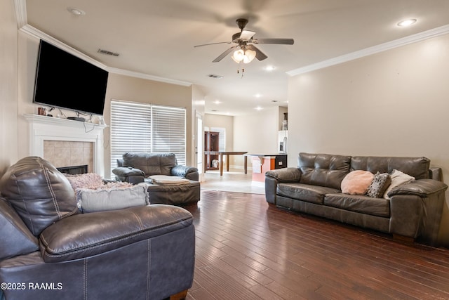 living room featuring ceiling fan, ornamental molding, dark hardwood / wood-style floors, and a tile fireplace