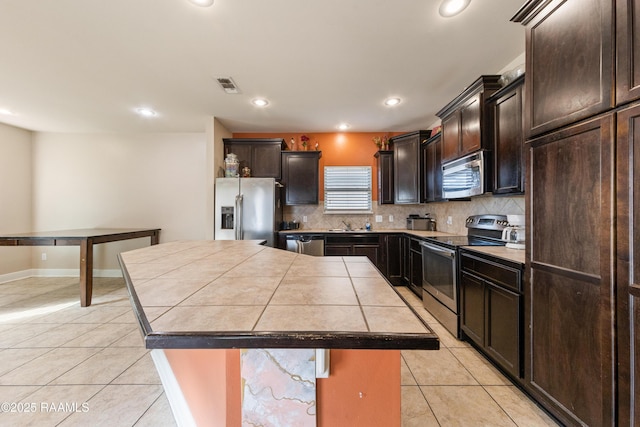 kitchen with light tile patterned floors, decorative backsplash, stainless steel appliances, and a kitchen island