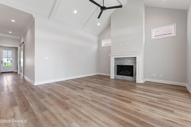 unfurnished living room featuring light hardwood / wood-style flooring, ceiling fan, high vaulted ceiling, a high end fireplace, and a barn door