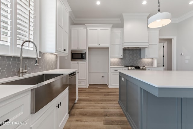 kitchen featuring white cabinetry, appliances with stainless steel finishes, decorative light fixtures, and custom range hood