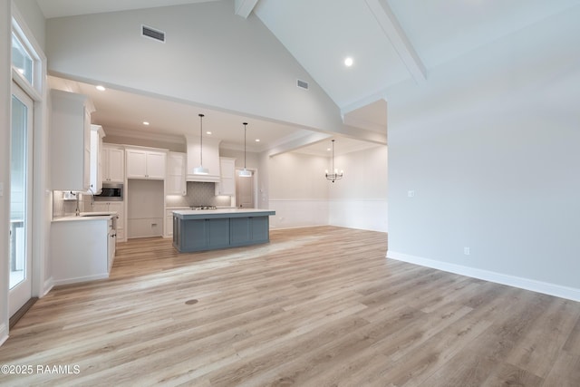 kitchen featuring white cabinetry, decorative light fixtures, a center island, stainless steel microwave, and beam ceiling