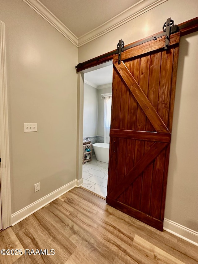 hallway with crown molding, a barn door, and light hardwood / wood-style flooring