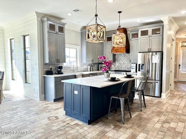 kitchen featuring sink, stainless steel fridge with ice dispenser, ornamental molding, a kitchen island, and pendant lighting