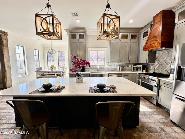 kitchen featuring premium range hood, an inviting chandelier, stainless steel appliances, a center island, and decorative light fixtures