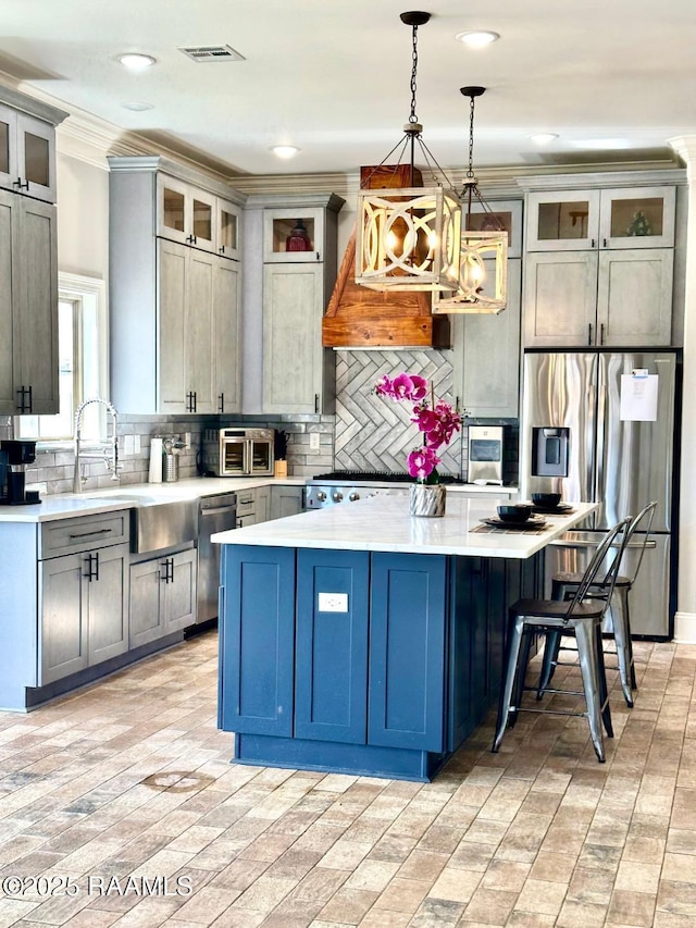 kitchen featuring crown molding, hanging light fixtures, appliances with stainless steel finishes, a kitchen island, and backsplash