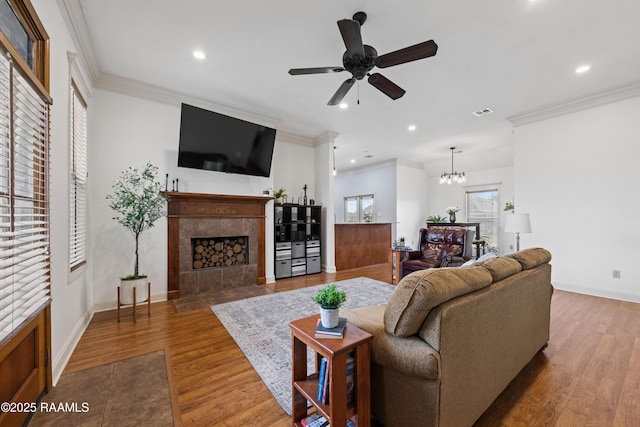 living room featuring hardwood / wood-style flooring, crown molding, a tiled fireplace, and ceiling fan with notable chandelier