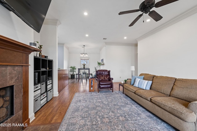 living room with ceiling fan with notable chandelier, hardwood / wood-style floors, a tile fireplace, and crown molding