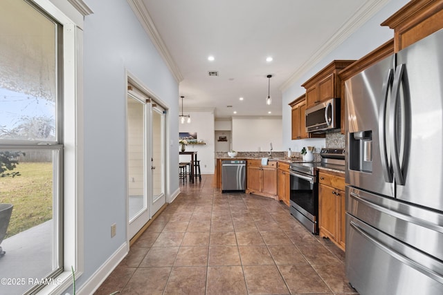 kitchen with a wealth of natural light, hanging light fixtures, dark tile patterned floors, appliances with stainless steel finishes, and ornamental molding