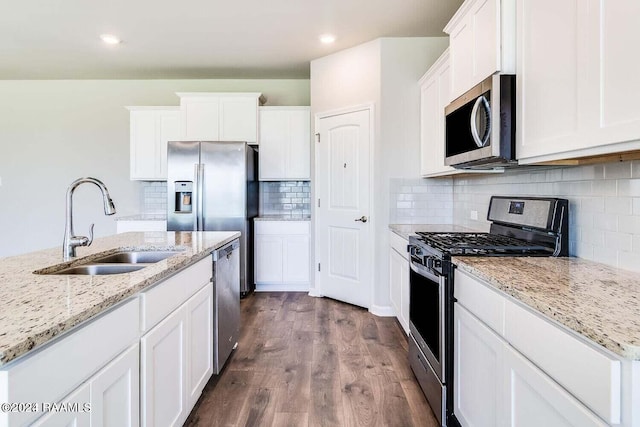 kitchen with stainless steel appliances, white cabinetry, light stone countertops, and sink