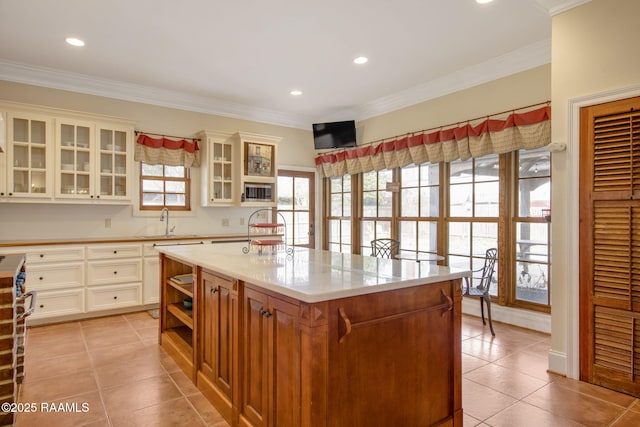 kitchen with ornamental molding, an island with sink, and light tile patterned floors