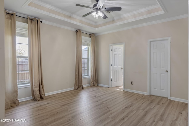 empty room with a tray ceiling, light wood-type flooring, and ornamental molding