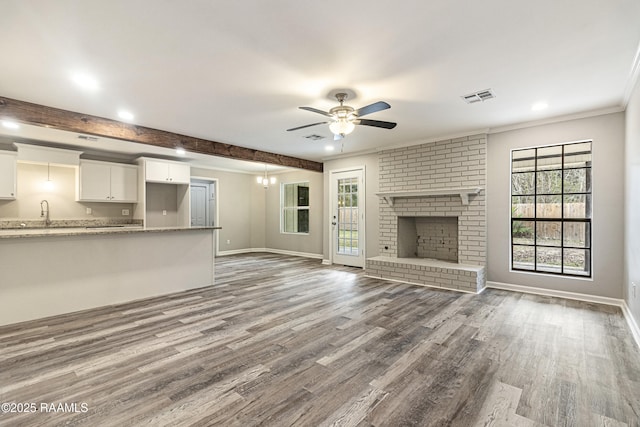 unfurnished living room with beamed ceiling, wood-type flooring, a brick fireplace, and ceiling fan