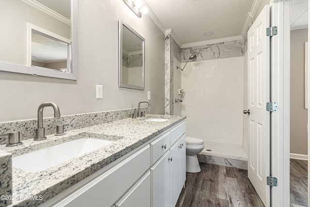 bathroom featuring crown molding, hardwood / wood-style floors, tiled shower, vanity, and toilet