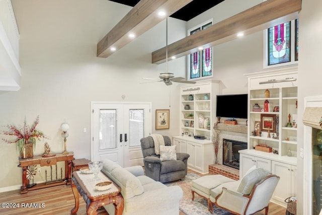 living room with a towering ceiling, a brick fireplace, ceiling fan, beam ceiling, and light hardwood / wood-style floors