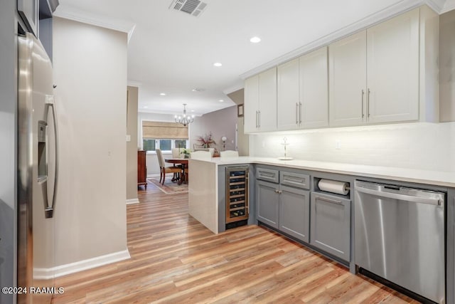 kitchen featuring hanging light fixtures, gray cabinets, appliances with stainless steel finishes, kitchen peninsula, and beverage cooler