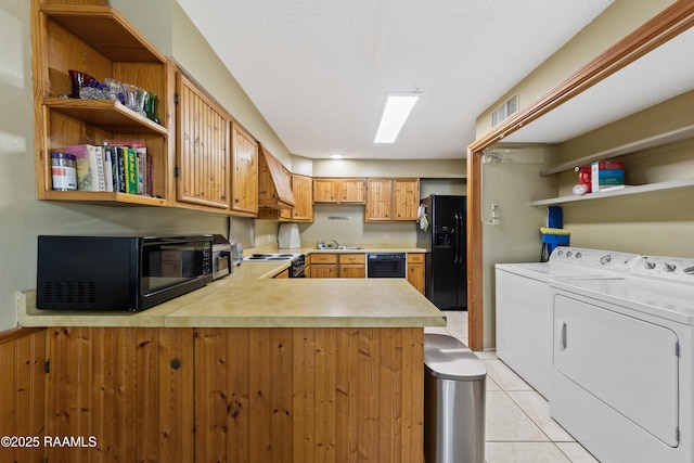 kitchen with kitchen peninsula, custom exhaust hood, light tile patterned floors, black appliances, and washing machine and clothes dryer