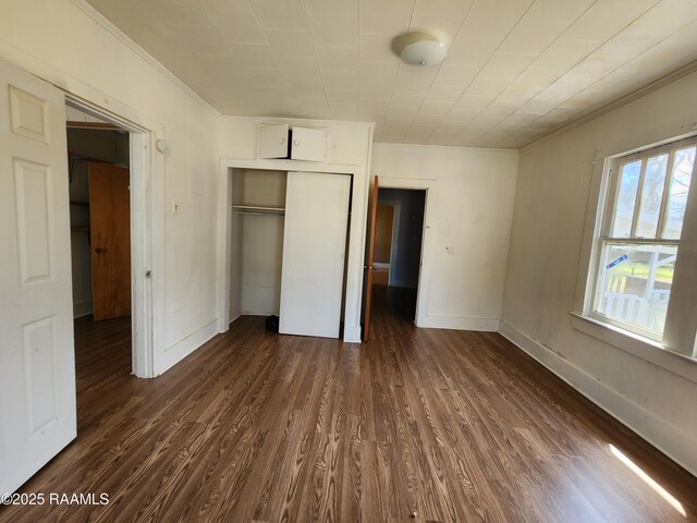 unfurnished bedroom with a closet, dark wood-style flooring, ornamental molding, and baseboards